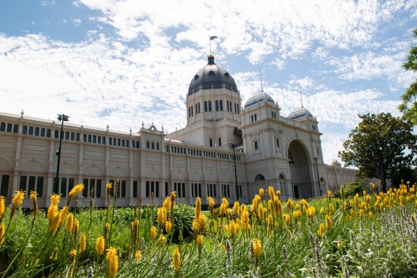 Image shows the exterior of the Royal Exhibition Building. Orange flowers can be seen outside the building.   
